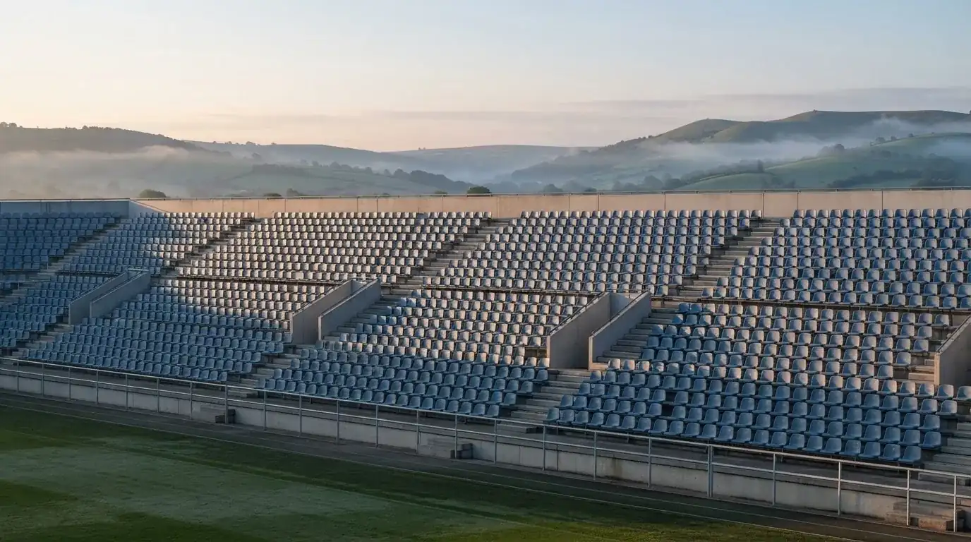 Ein leeres Stadion im Morgenlicht mit Blick auf die Sitzreihen, im Hintergrund Hügel und aufsteigender Nebel.