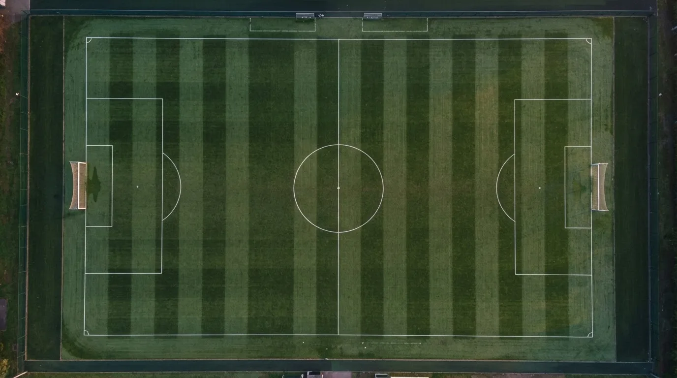 Ein Fussballplatz von oben gesehen, die Linien bilden ein helles Muster auf dem Rasen, Drohnenperspektive in der Morgendämmerung.