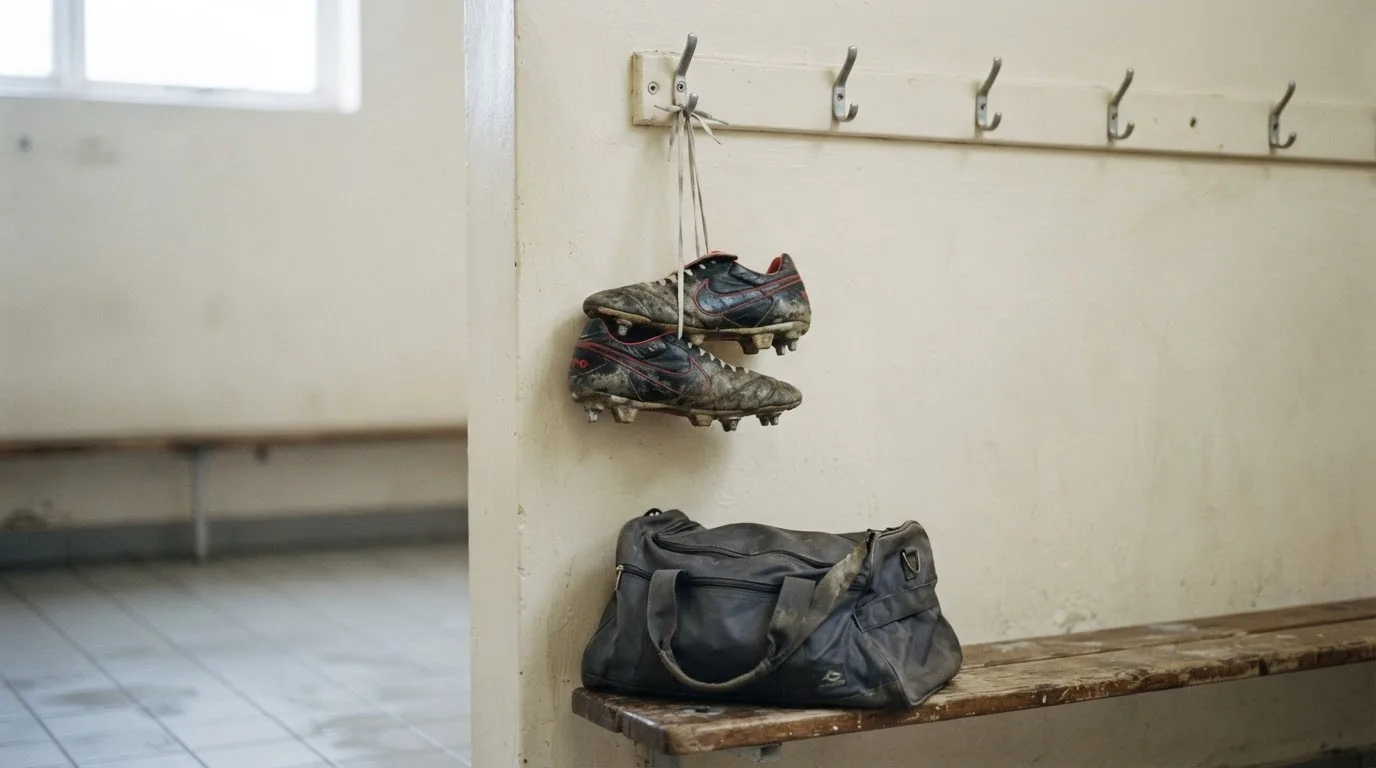 Ein Paar Fussballschuhe hängt an einem Haken in einer ruhigen Umkleide, darunter steht eine Sporttasche auf einer Holzbank.
