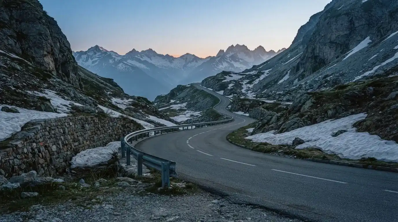 Ein Bergpass in den Schweizer Alpen mit leerer Strasse und Schneeresten am Rand im ersten Frühlicht.