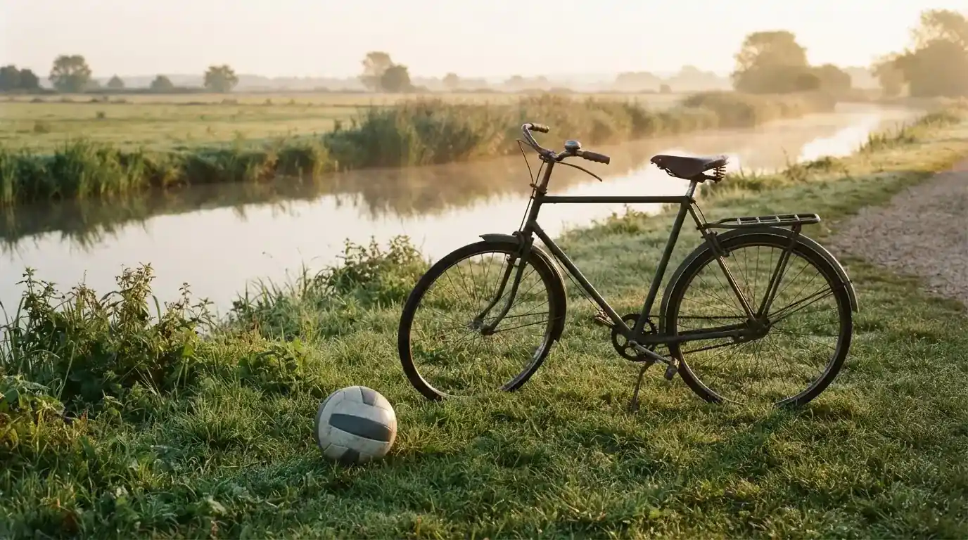 Ein Fussball liegt auf einer Wiese neben einem Fahrrad, im Hintergrund ein Kanal im Morgenlicht